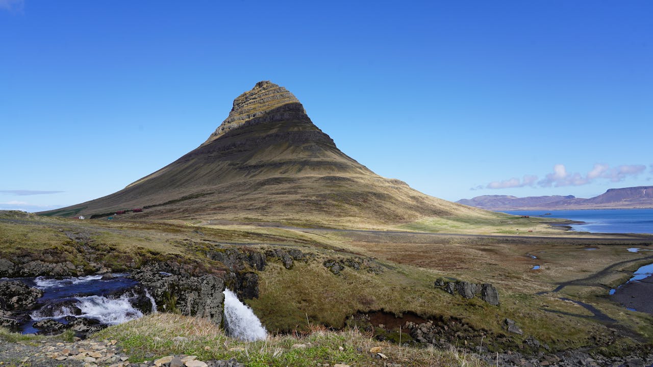 Capture of Kirkjufell Mountain in Iceland with blue skies, highlighting its unique shape and natural surroundings.
