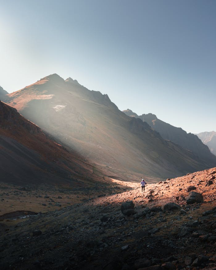 A lone hiker traverses a scenic mountain landscape in Huarochirí, Peru, under the clear day sky.